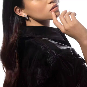 Woman wearing a black jacket and diamond earrings with a neutral background
