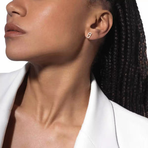 Close-up of a person wearing a gold earring with a clear gemstone on a white background