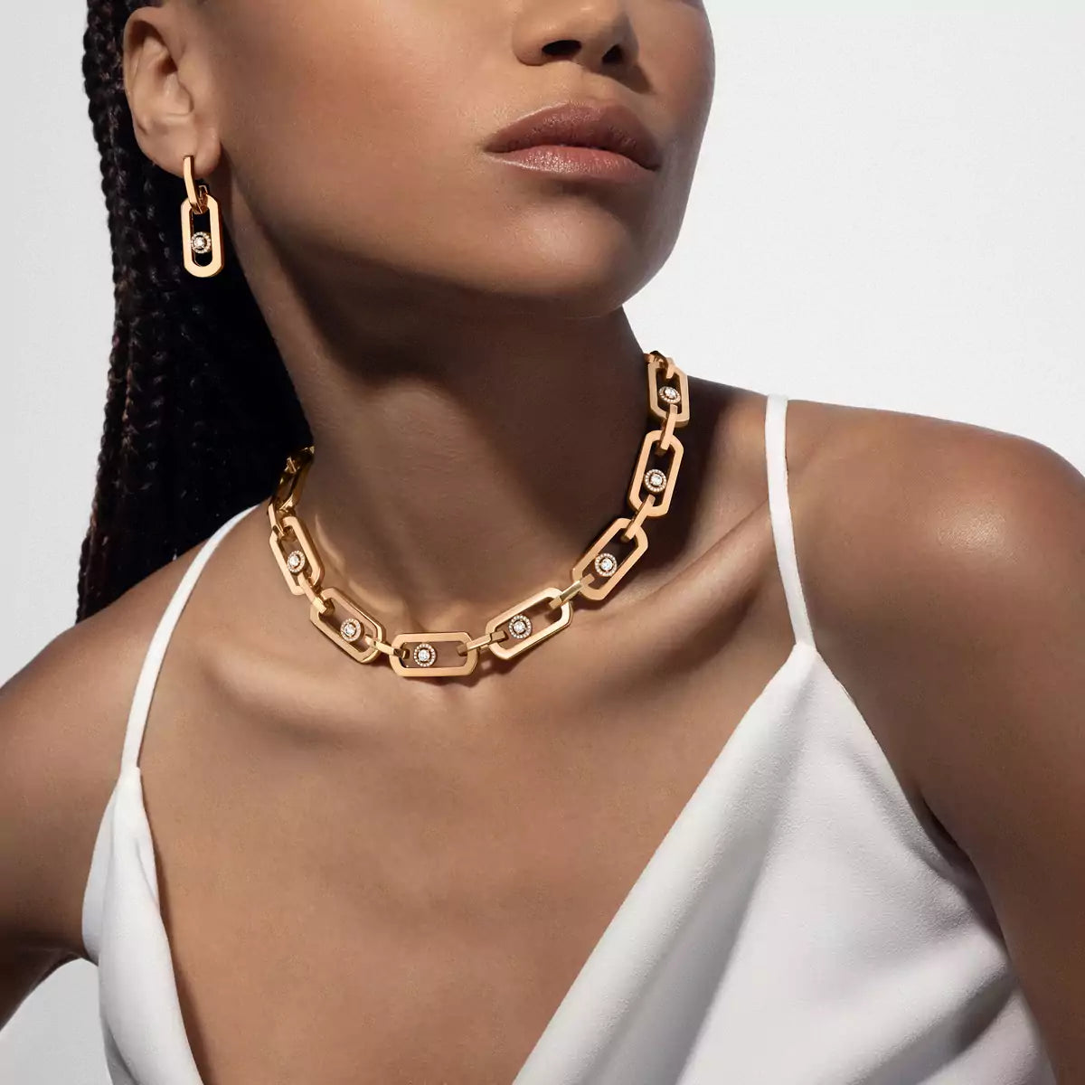 Woman wearing a gold chain necklace and earrings on a plain background