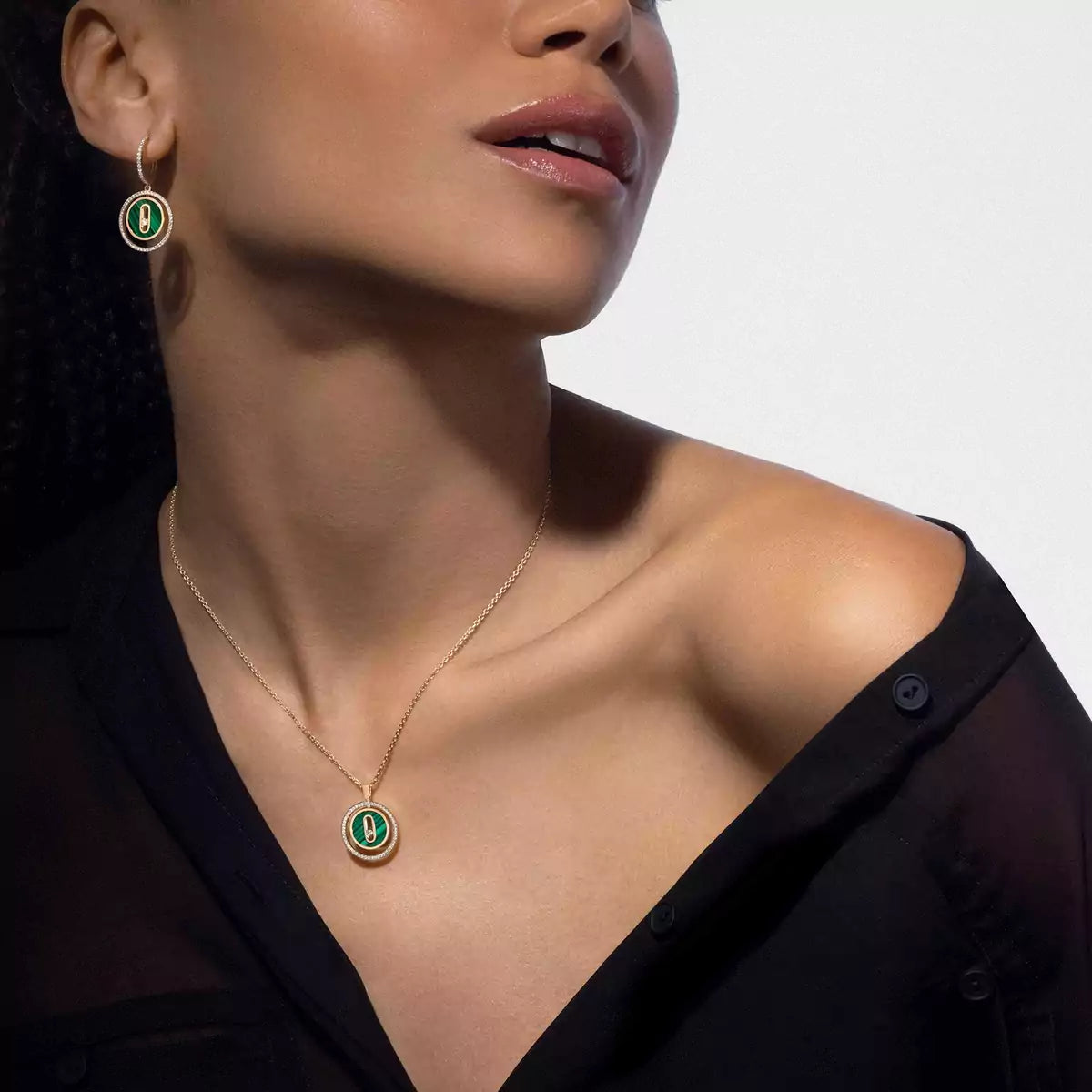 Close-up of a woman wearing a gold necklace with a green pendant on a plain background