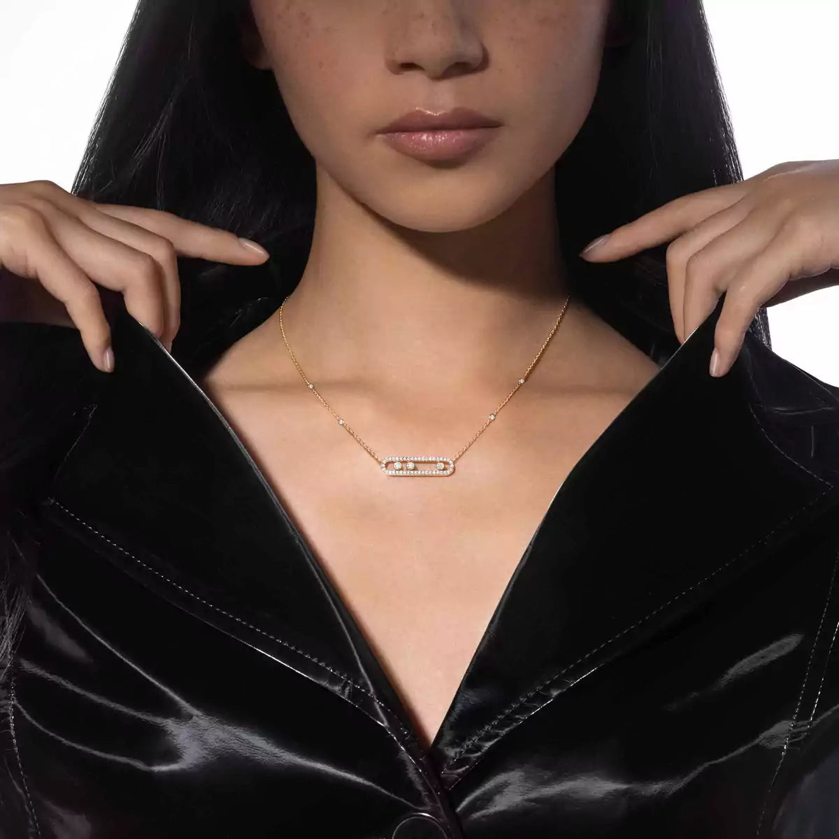 Woman wearing a gold necklace with a bar pendant against a black background