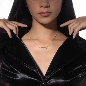 Woman wearing a gold necklace with a bar pendant against a black background