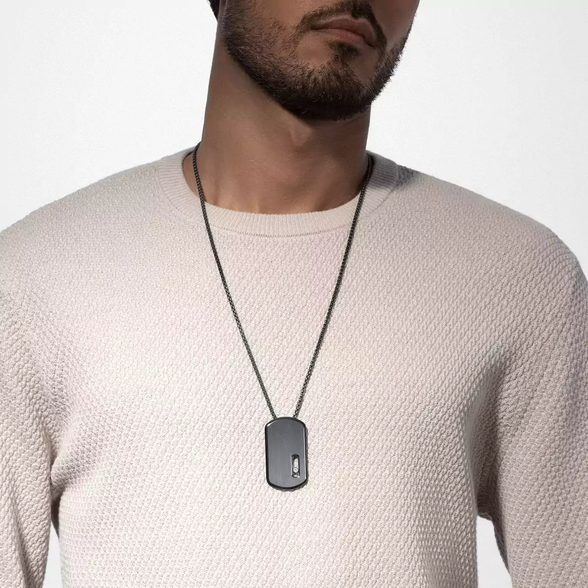 Man wearing a necklace with a dog tag on a plain background
