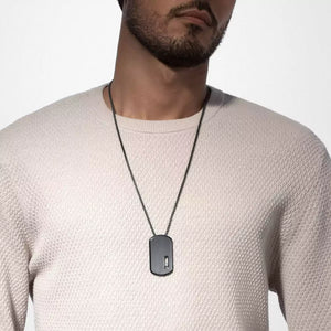 Man wearing a necklace with a dog tag on a plain background