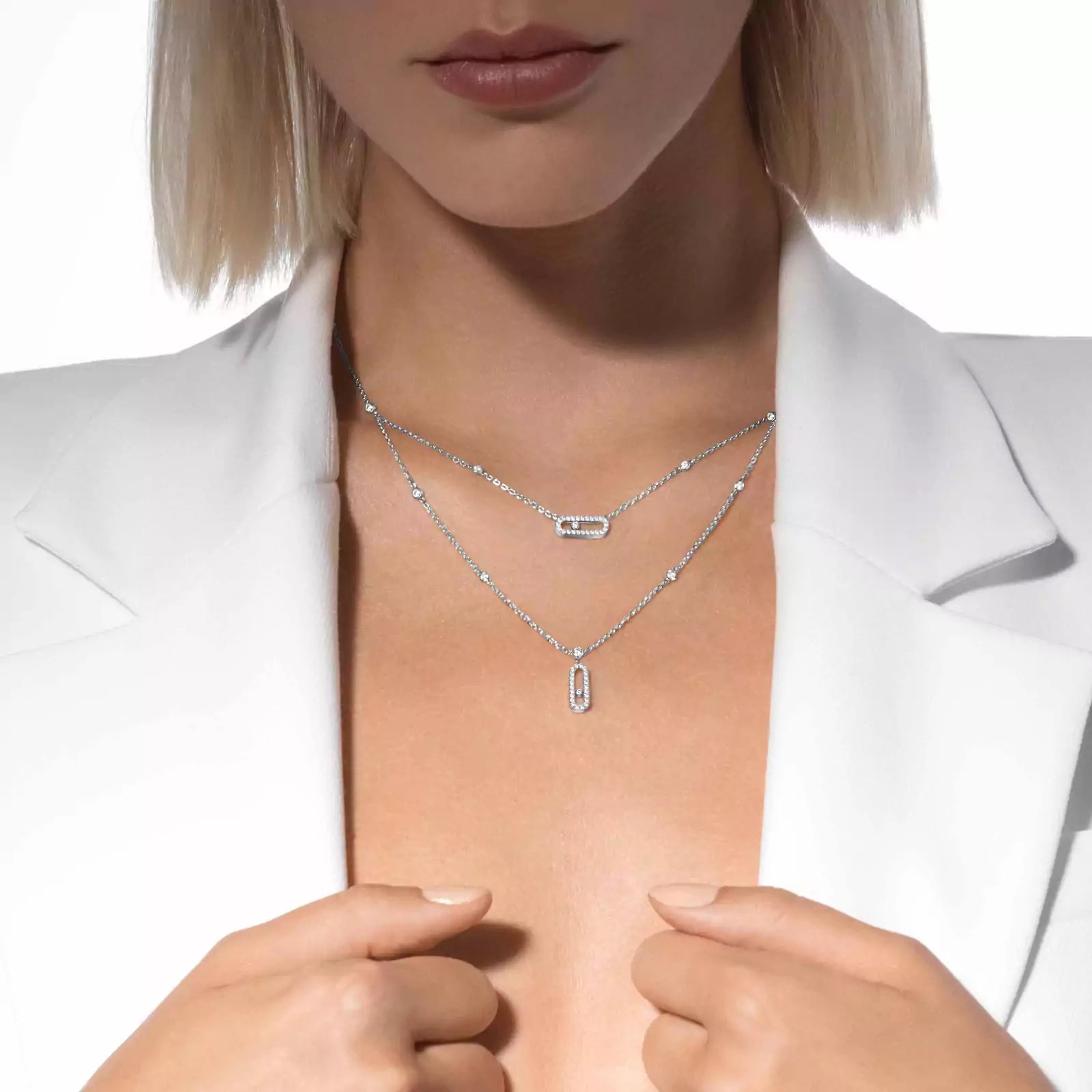 Close-up of a person wearing two silver necklaces on a white background