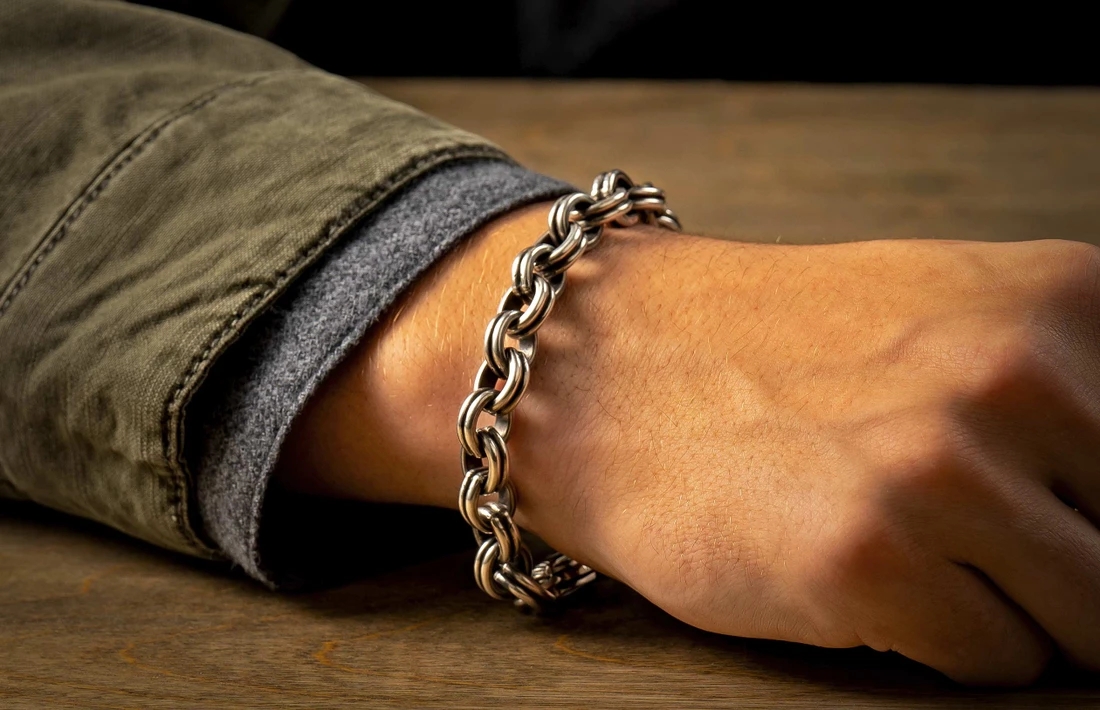 Silver rope-link bracelet on a wrist resting on a wooden table, olive jacket cuff visible