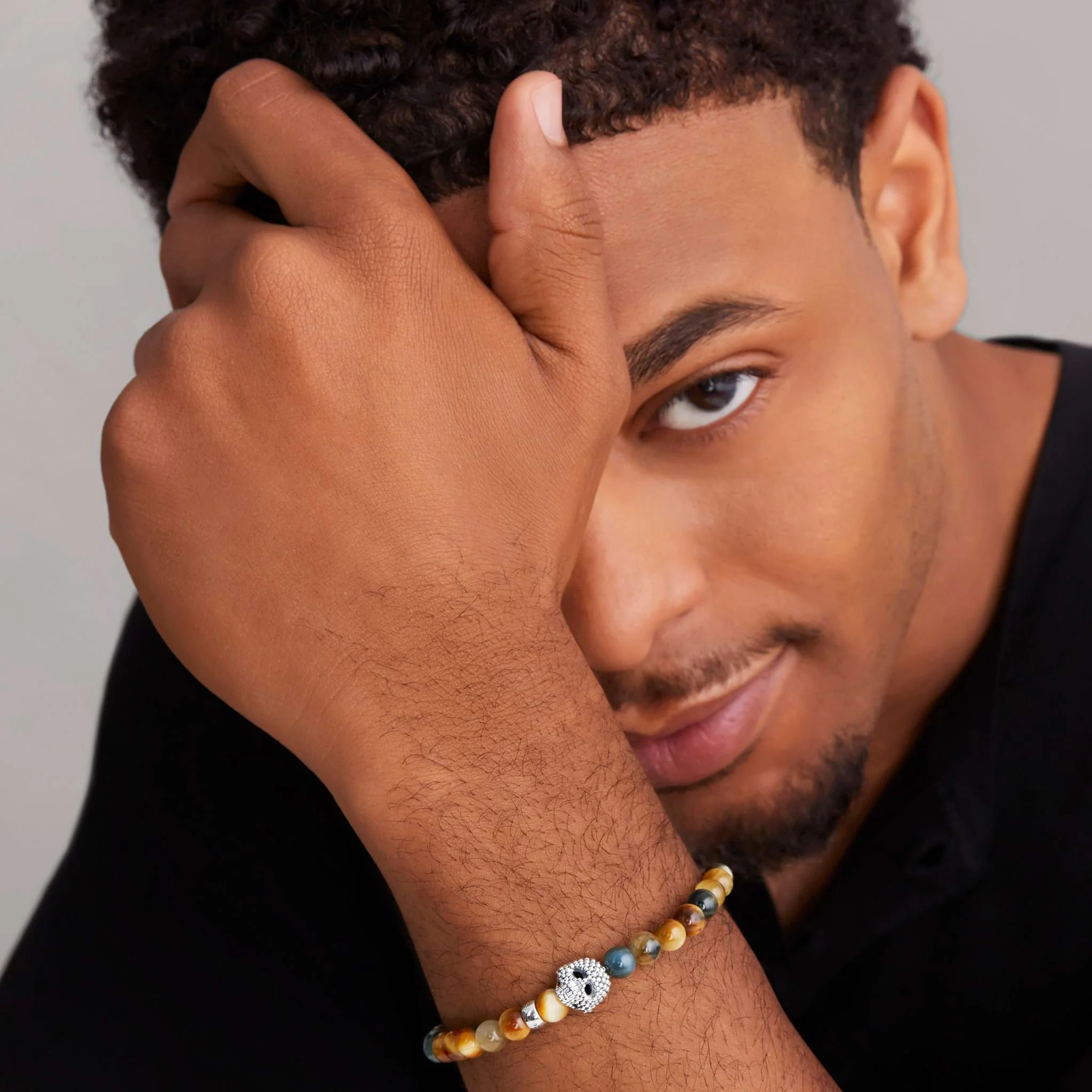 Close-up of wrist wearing Tigereye Skull bracelet with 6mm tigereye beads and sterling silver caviar skull on a model in a black shirt