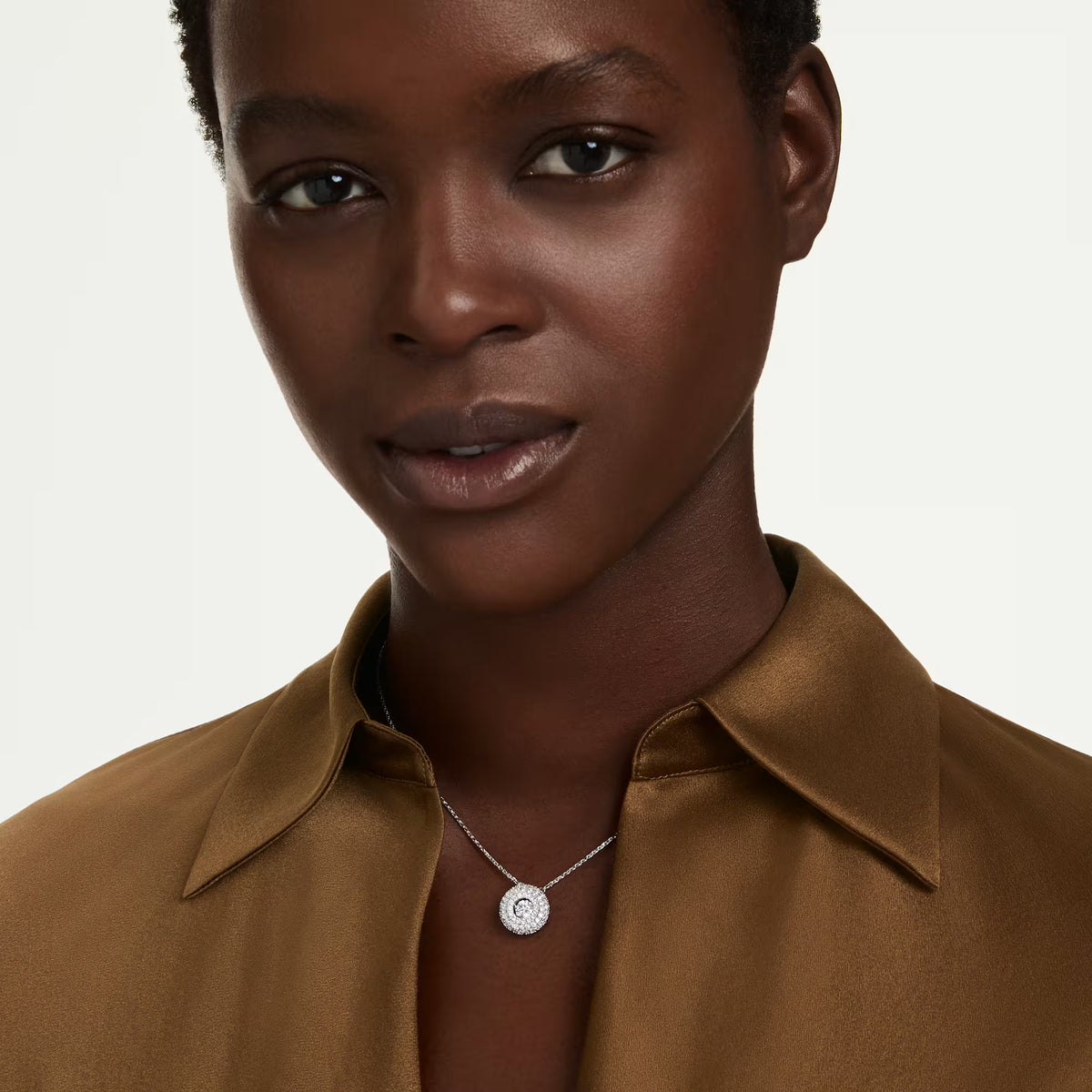 a model wearing a silver necklace with a round center stone on a white background
