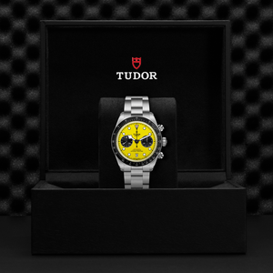 Tudor watch with yellow face and silver bracelet on a black display stand against a textured black background.