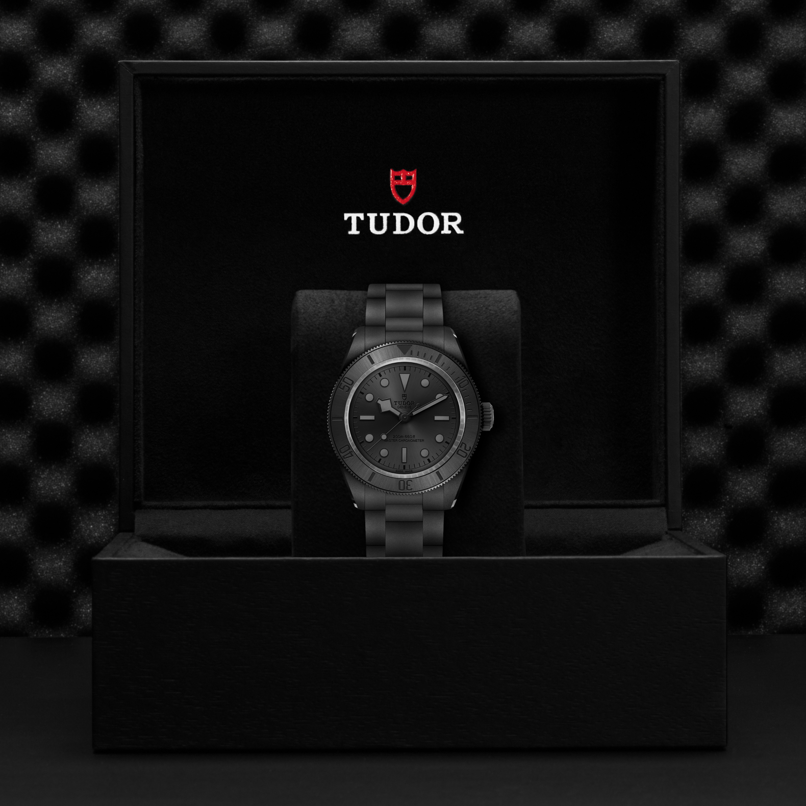 Tudor watch in a black box with the Tudor logo on a dark textured background