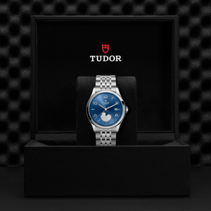 Front view of TUDOR 1926 Luna 39mm steel watch with blue sunburst dial, moonphase and date, steel bracelet in black box