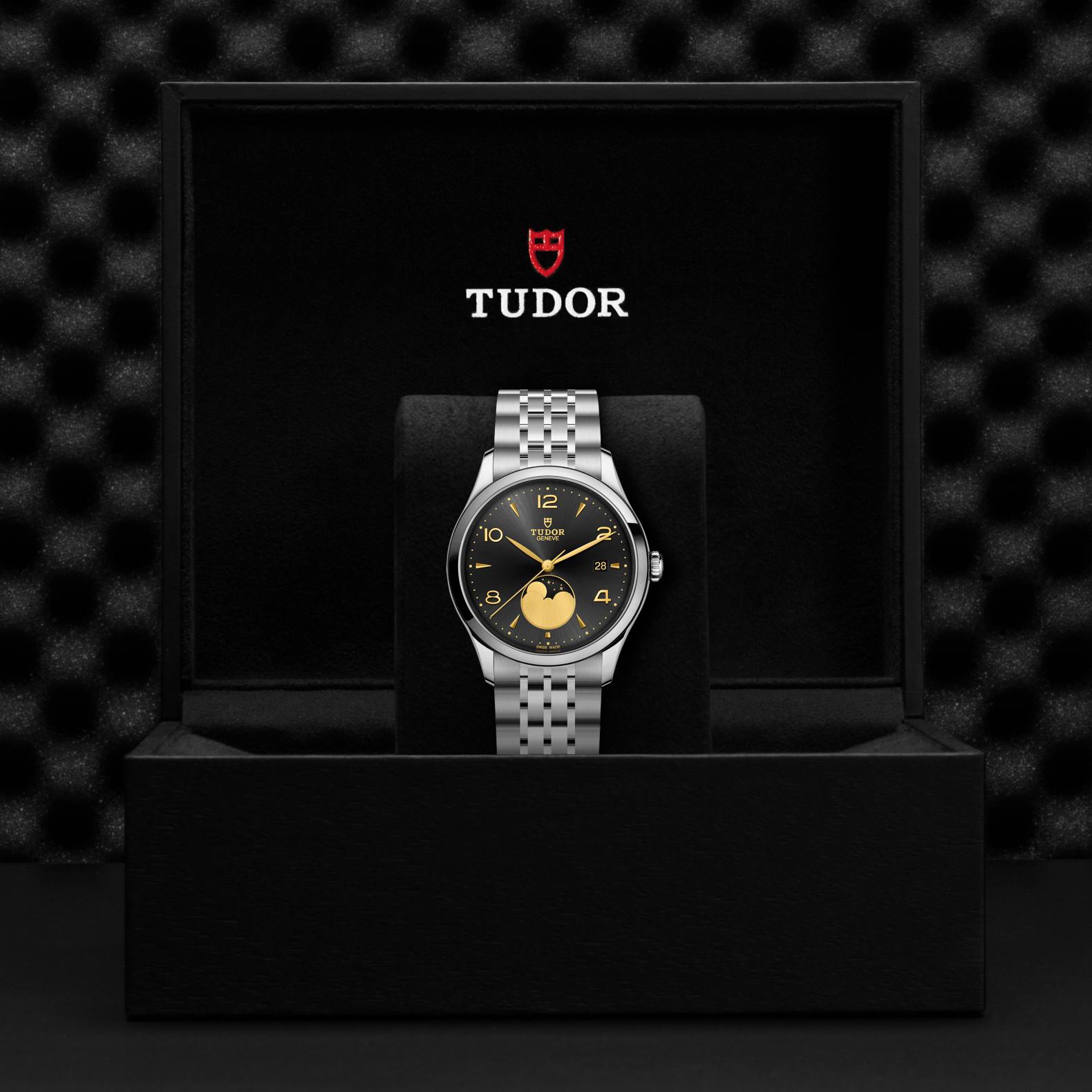 Front view of TUDOR 1926 Luna watch with black sunburst dial, gold numerals and moon phase, on steel bracelet in black Tudor box