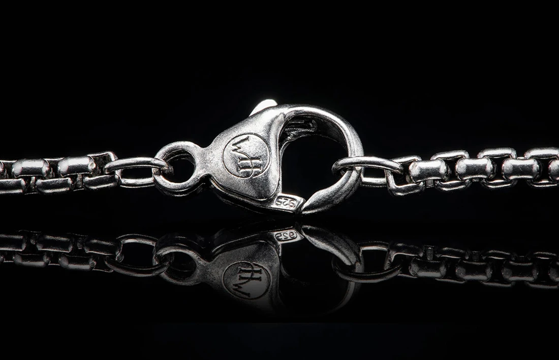 Close-up of William Henry Dino Pinnacle necklace showing sterling silver lobster clasp with WH logo and 925 stamp on black reflective background