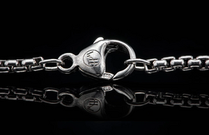 Close-up of William Henry Dino Pinnacle necklace showing sterling silver lobster clasp with WH logo and 925 stamp on black reflective background