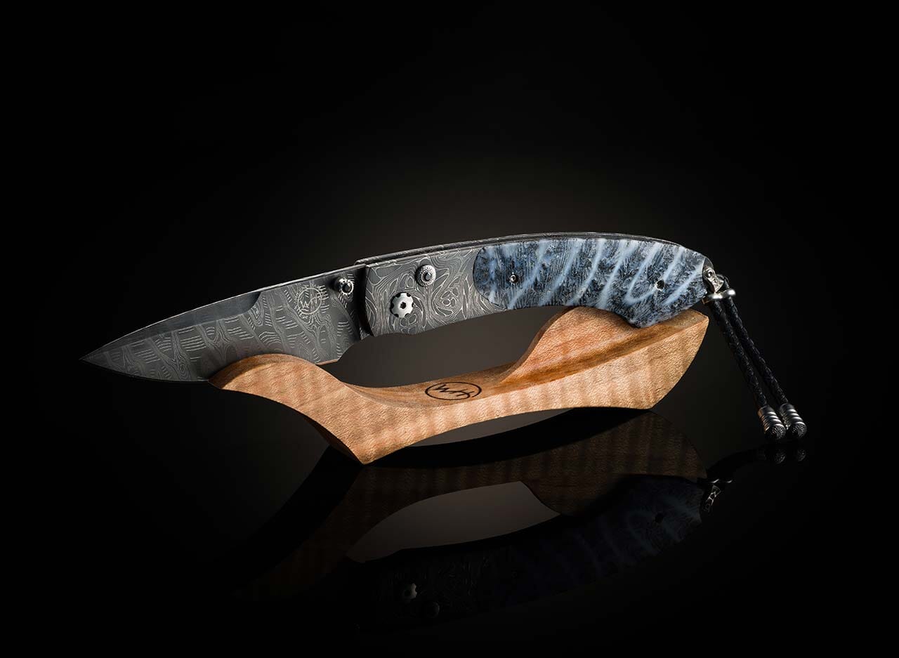 Folding knife with wooden handle and blue patterned blade on a black background