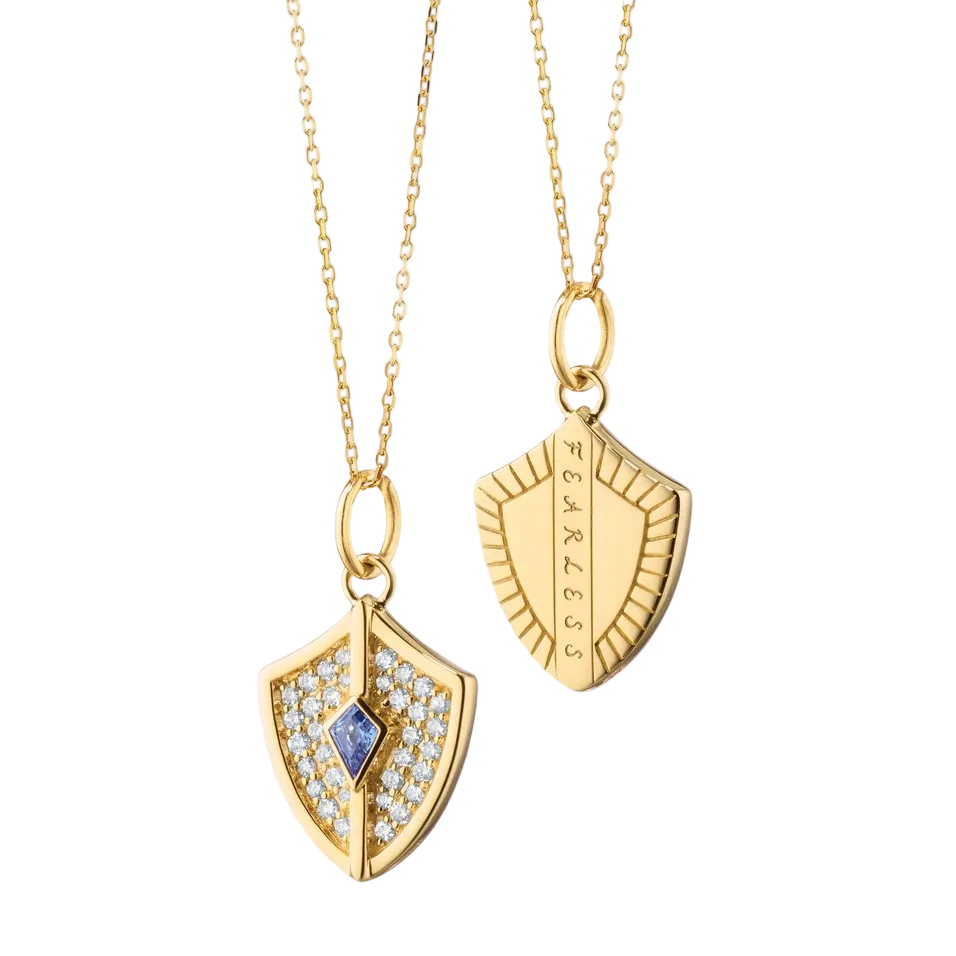 gold necklace with a shield charm with diamonds and blue sapphire in the center on a white background