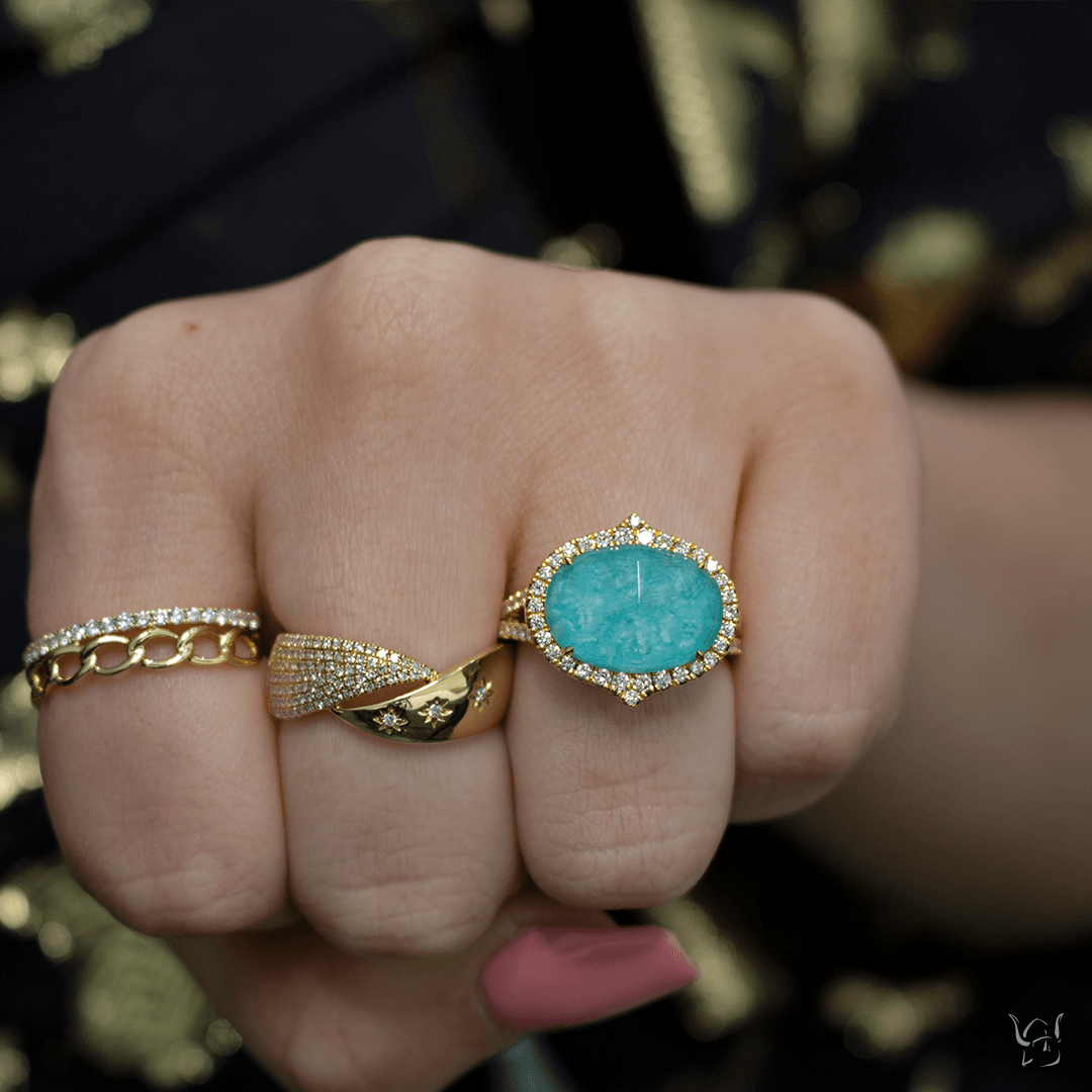 Hand wearing three gold rings: turquoise oval halo ring and diamond-accent star band on adjacent fingers
