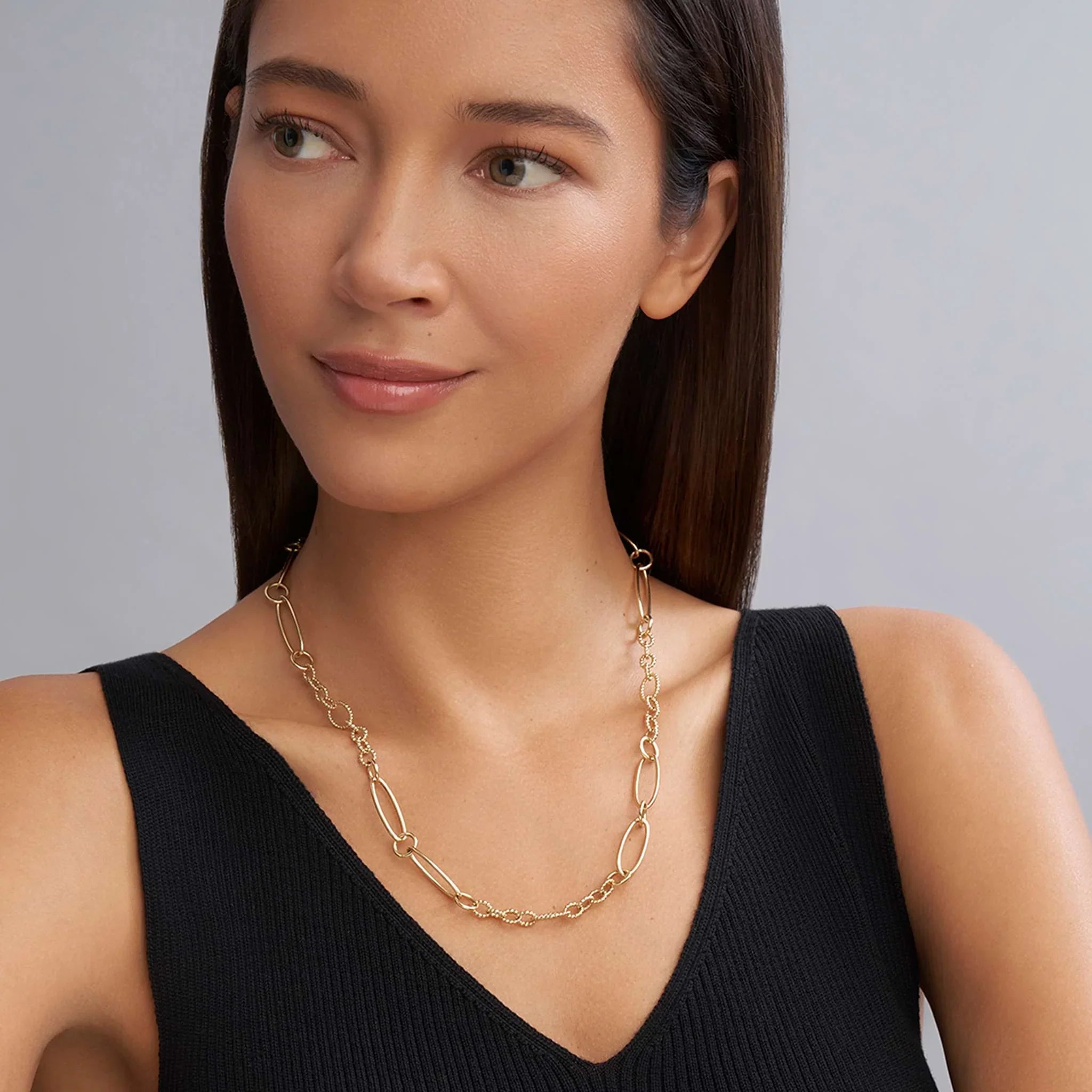 Front view of 18K gold link necklace with alternating large and small links worn by model in a black V-neck on gray background