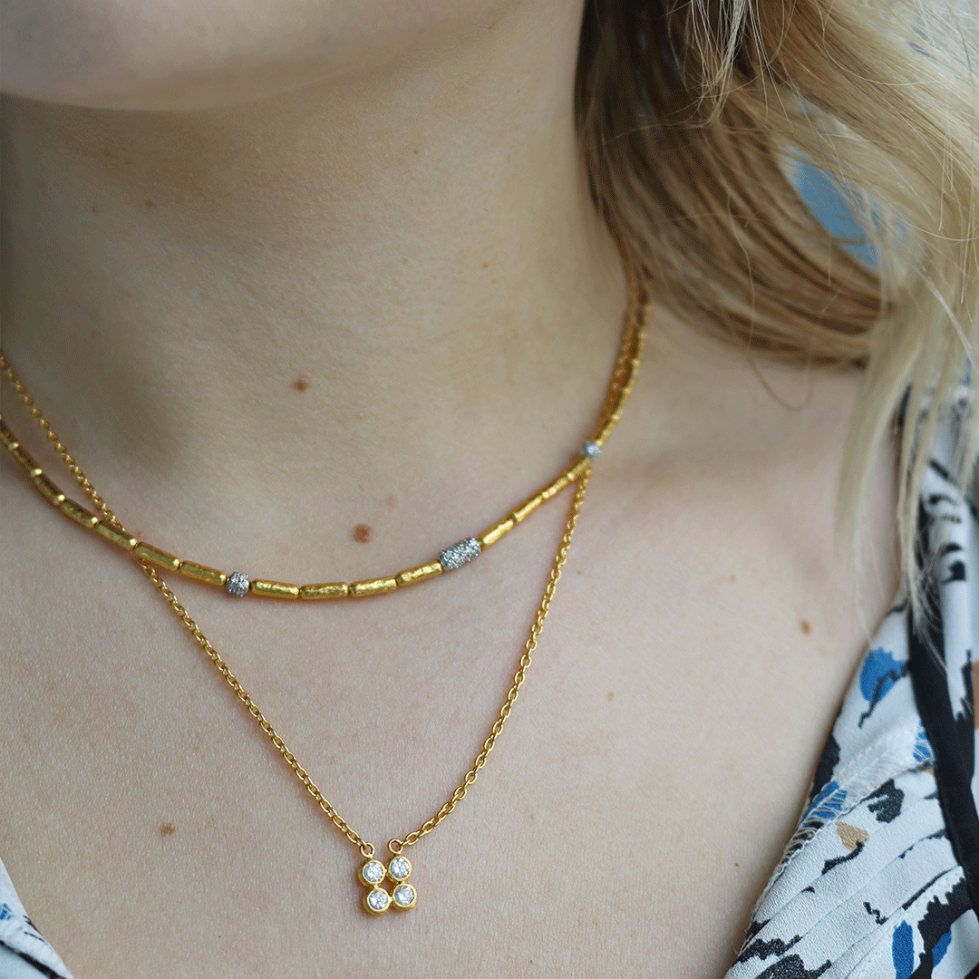 Close-up of model's neckline wearing Pointelle gold cluster necklace with three-diamond pendant layered with a gold chain