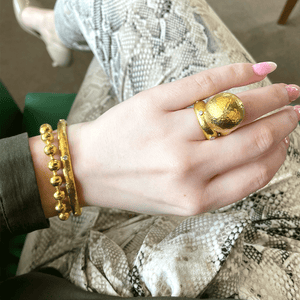 Close up of hand wearing gold and diamond band ring with hammered dome and small diamond on snakeskin pants