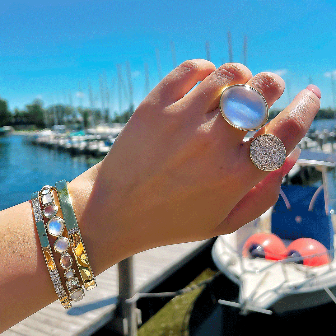 Close-up of wrist wearing Medium 3-station bangle in 18K yellow gold with three diamond stations, marina background