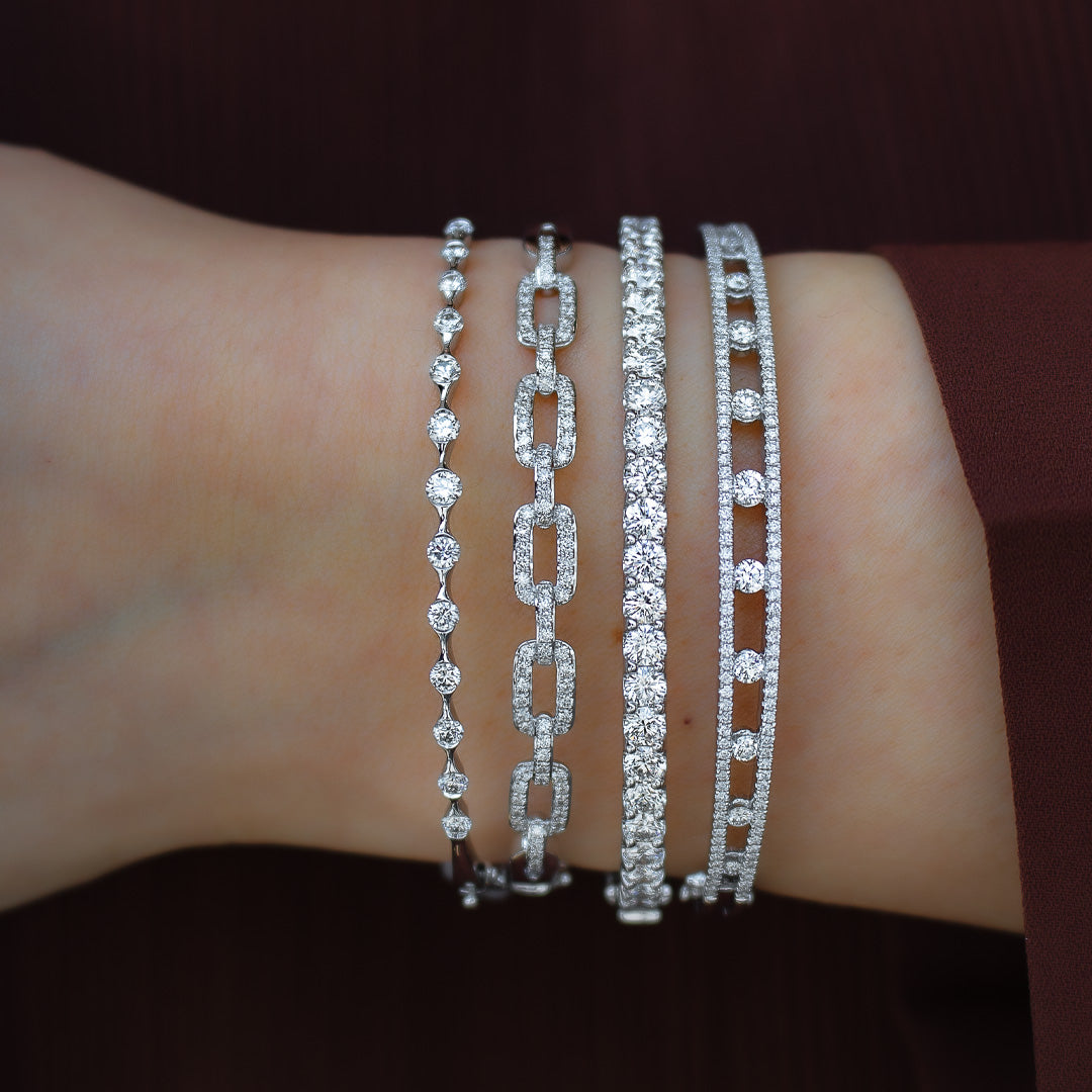 Close-up of wrist wearing 0.92ctw white gold diamond bangle and three stacked diamond bracelets against burgundy sleeve