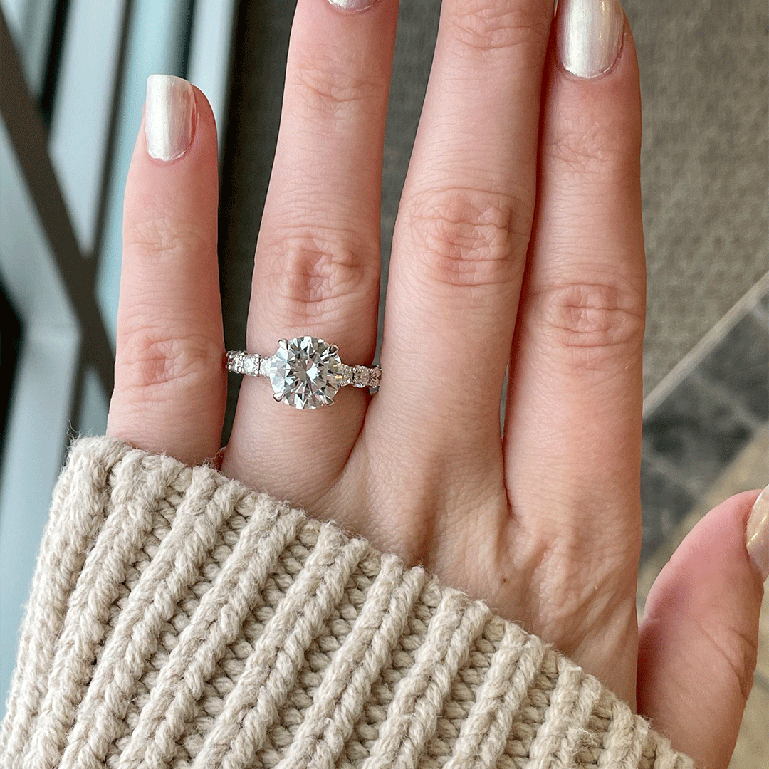 Top view of 1.18ctw diamond engagement ring showcasing large round center stone and diamond-set band on a hand with beige knit sleeve