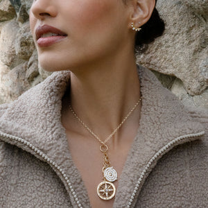 Close-up of Design Your Own yellow gold charm chain necklace showing hinged links and compass charms on model in fleece