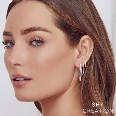 Woman wearing three diamond V hoop earrings; SHY CREATION logo at bottom right.