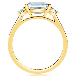 Side view of .49ctw emerald-cut diamond engagement ring showing three-stone 14K yellow gold setting on white background