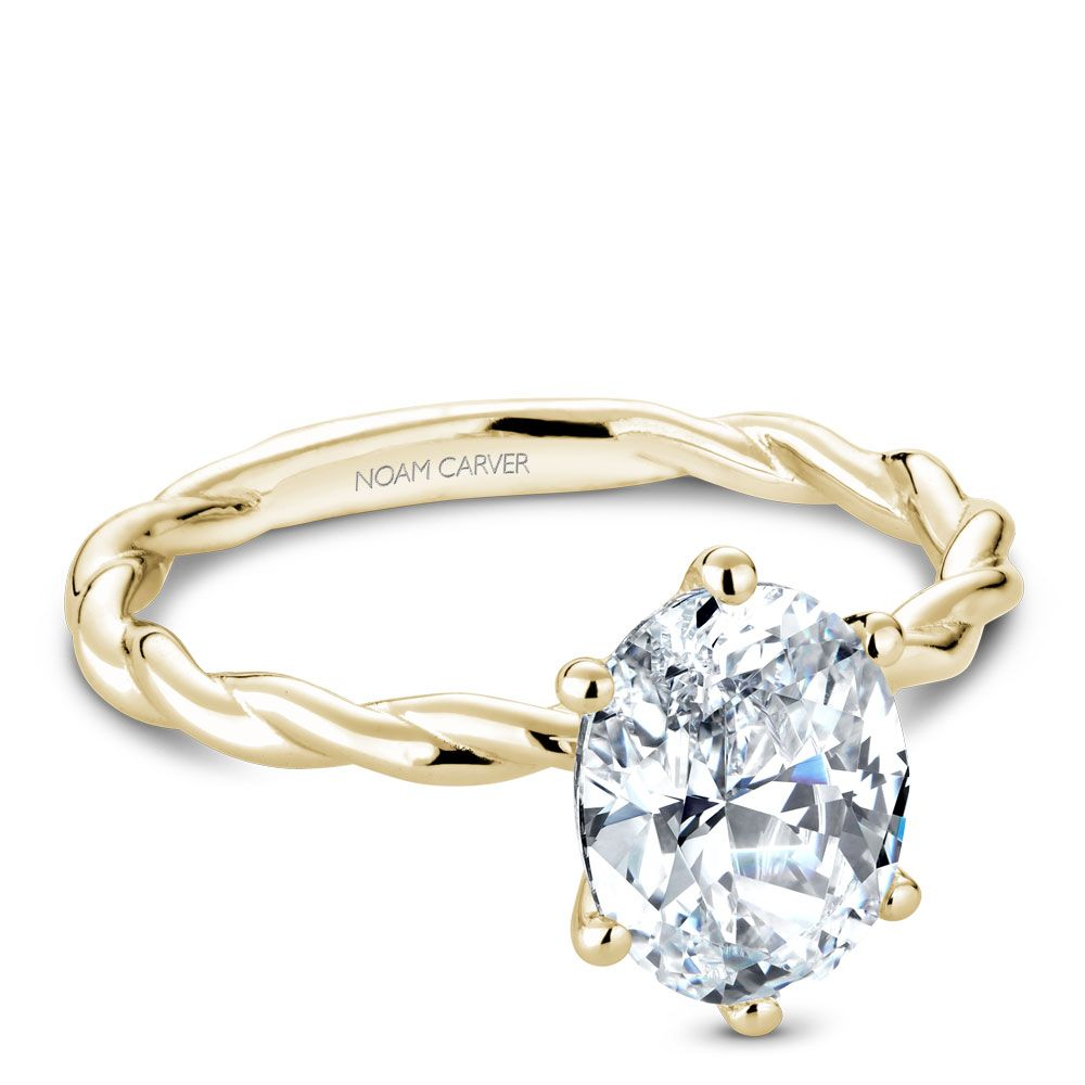 Angled view of 18K yellow gold twist-band ring with oval diamond solitaire and visible NOAM CARVER engraving on white