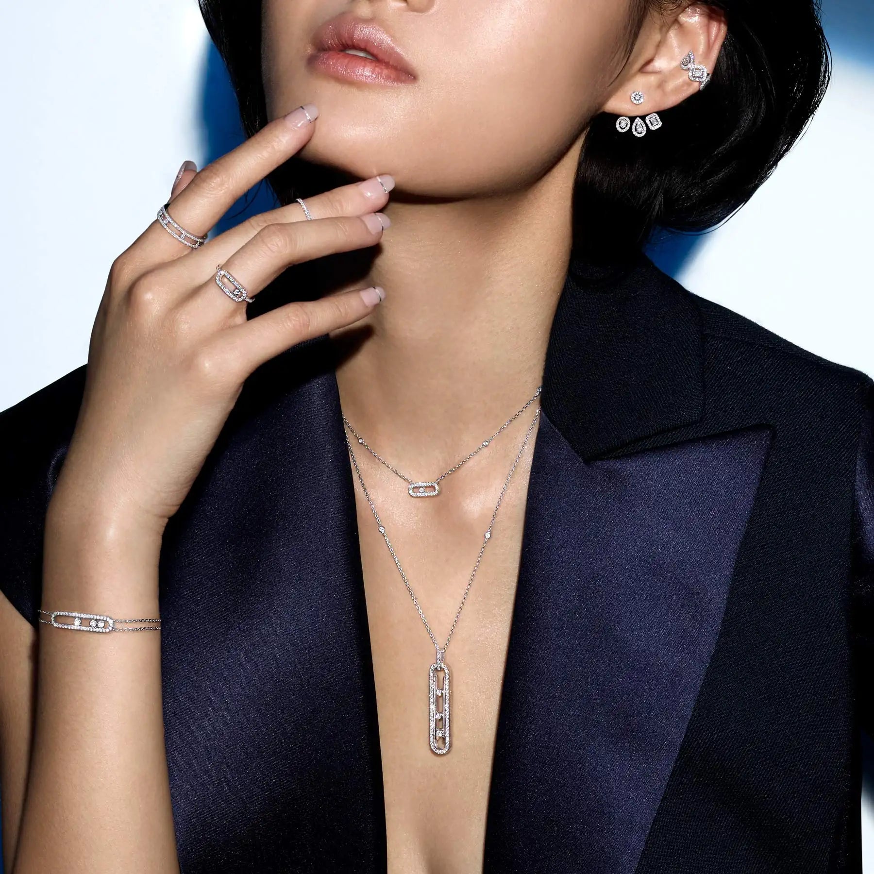 Woman wearing a black blazer and diamond rings, bracelet, earrings and necklaces on a white background