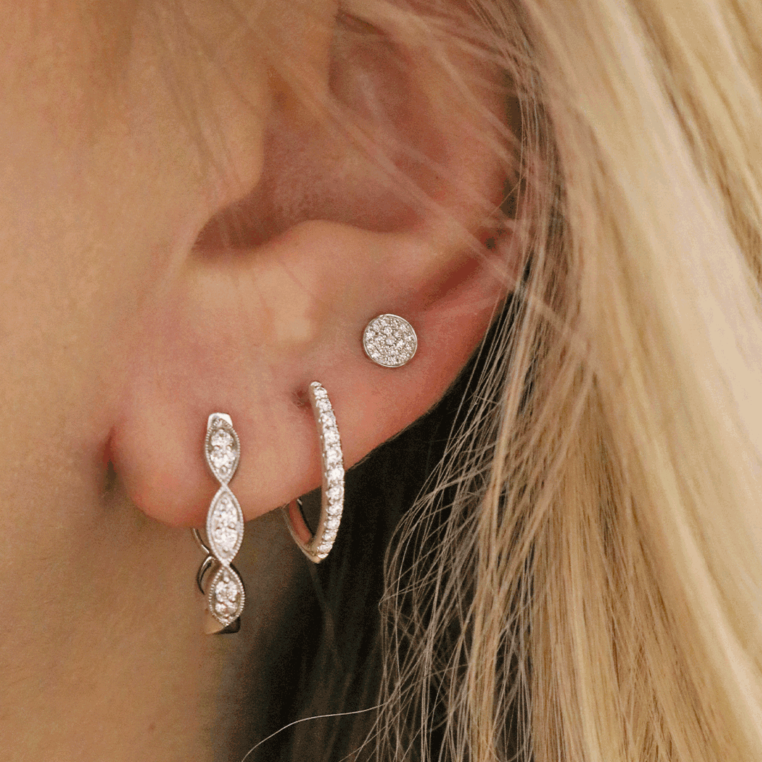 Ear wearing three white-gold diamond earrings: pavé round stud, small diamond hoop, and marquise-link drop.